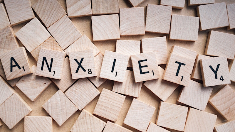 The word “anxiety” spelled out with wooden Scrabble tiles on a flat surface, representing mental health challenges.