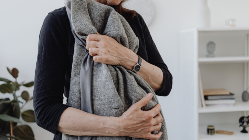 Woman hugging a grey jacket, holding onto it in remembrance of her late husband, expressing grief and loss.