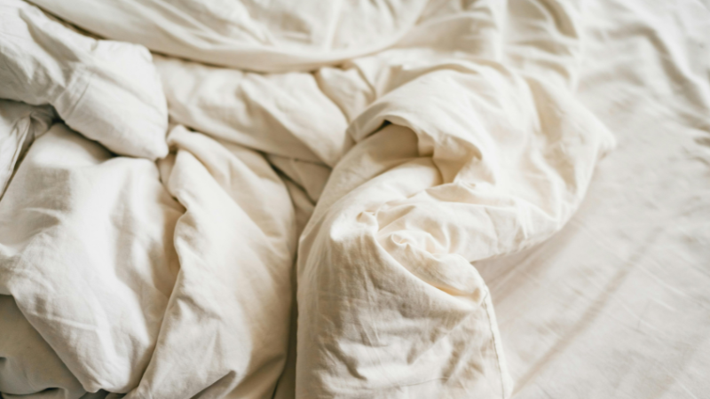 Unmade bed with soft white cotton sheets and covers, creating a cozy and relaxed bedroom atmosphere.