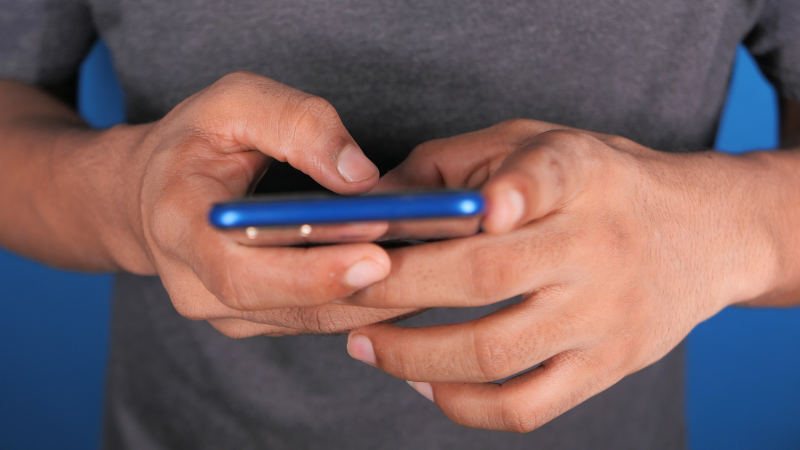 Man’s hands typing on a smartphone, representing digital communication and access to mental health support.