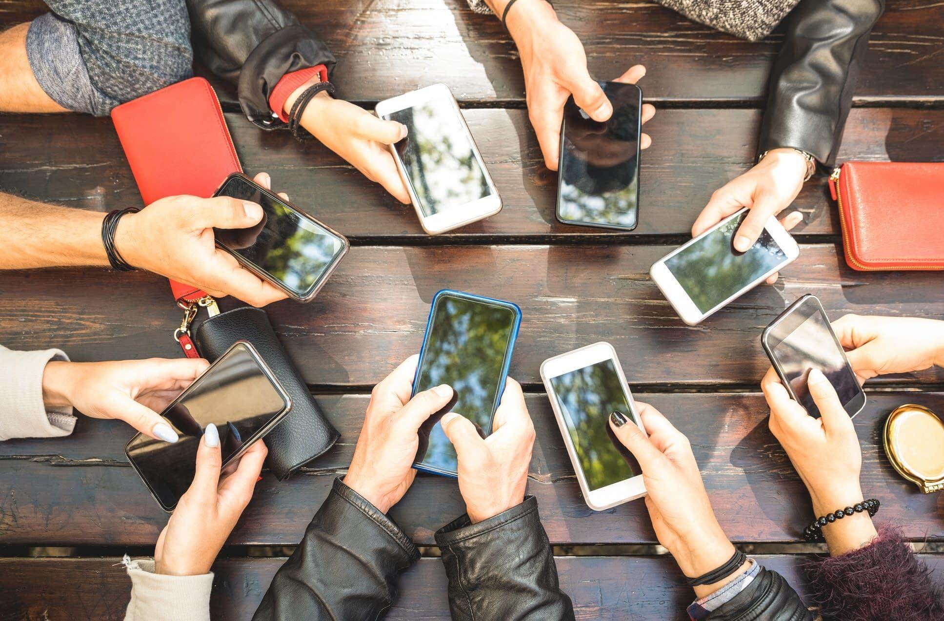 Group of Friends Sitting At Table with Mobile Phones Out