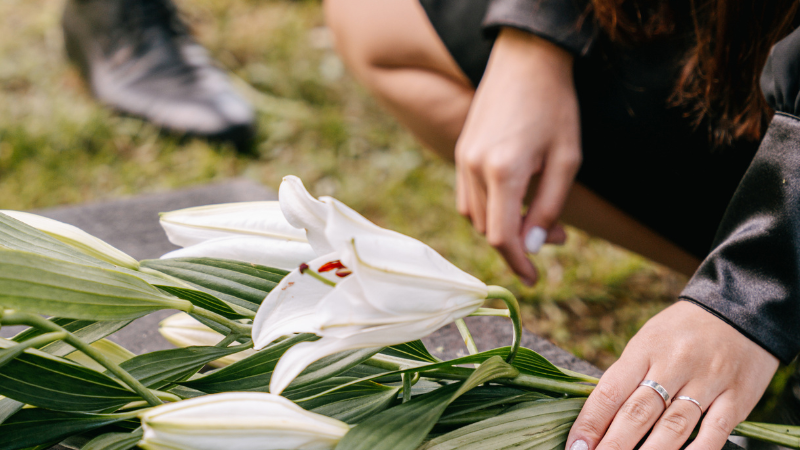 Lady placing white lilies on a grave, honouring a loved one
