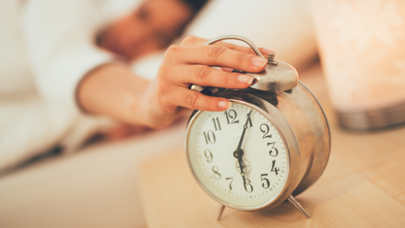 Woman lying in bed turning off a 6am alarm clock, enjoying a lie-in