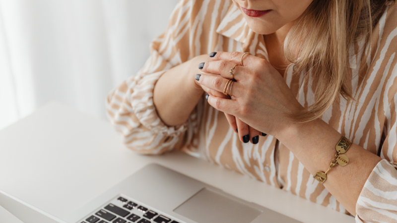 A woman sitting at a desk with her hands held together over a laptop.