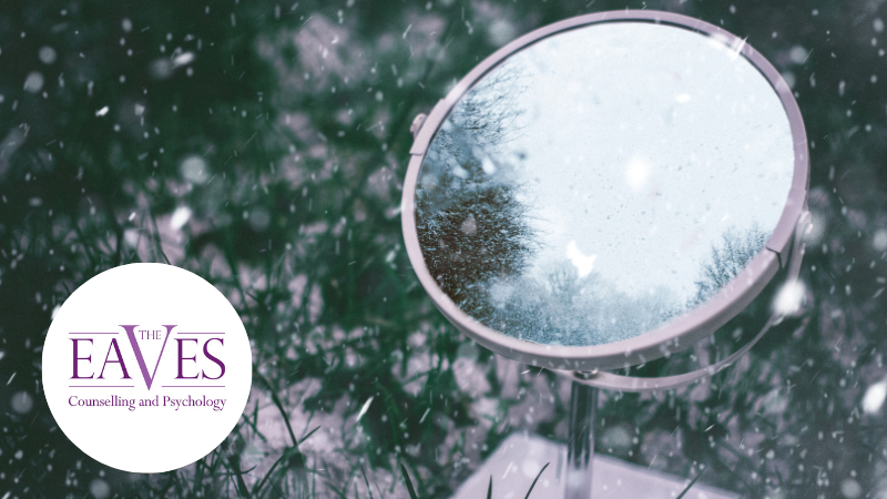 A round mirror resting on grass with raindrops on its surface.