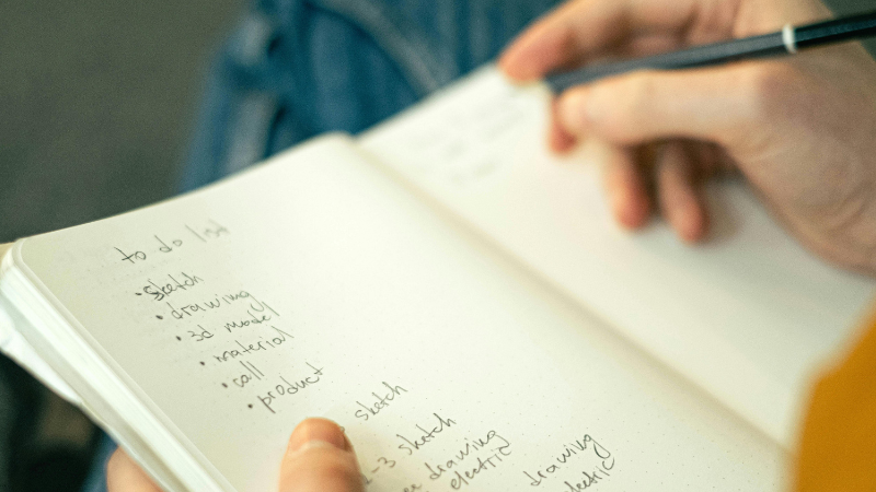 Man writing a to-do list with a pencil in a notepad, illustrating creative writing and reflective practice at The Eaves Counselling and Psychology.