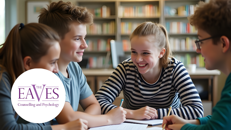 Two teenage girls and two teenage boys chatting over books in a school library, representing adolescent mental health and peer connection – The Eaves Counselling and Psychology