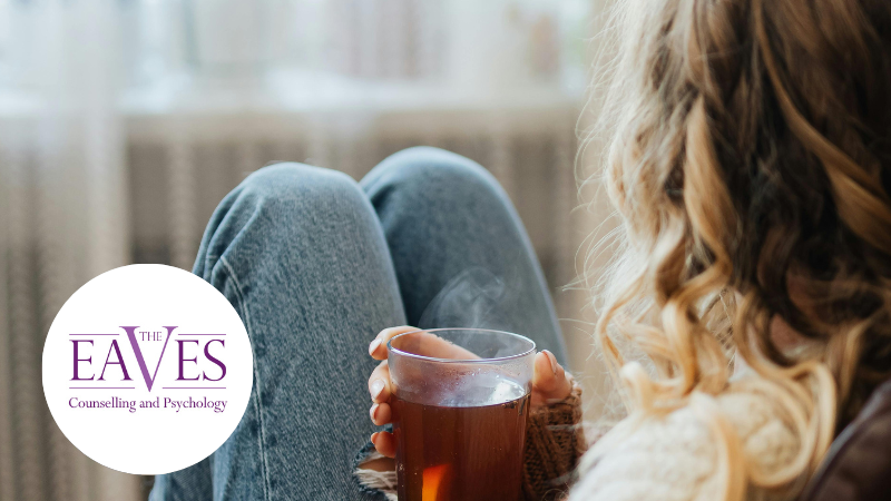 Girl in jeans holding a cup of tea in her living room, enjoying a moment of calm and self-care – The Eaves Counselling and Psychology