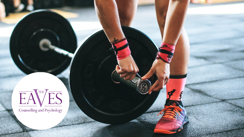 A person adjusting weights on a barbell, representing physical training, pressure, and the mental health challenges faced by elite athletes