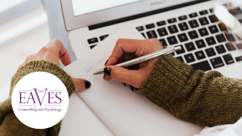 Woman in green jumper writing notes next to a laptop, representing focus, reflection, and understanding OCD – The Eaves Counselling and Psychology