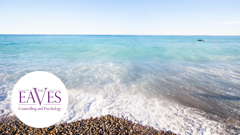 A serene beach scene with The Eaves Counselling and Psychology logo in the bottom left, representing relaxation, mental wellbeing, and the benefits of taking a work break