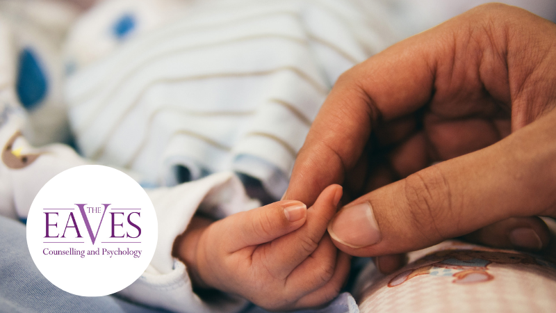Parent gently holding a newborn baby’s hand on a striped blanket, symbolising early bonding and new parenthood