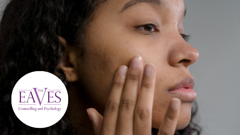 Woman touching her cheek, concerned about acne, illustrating the link between skin and mental health