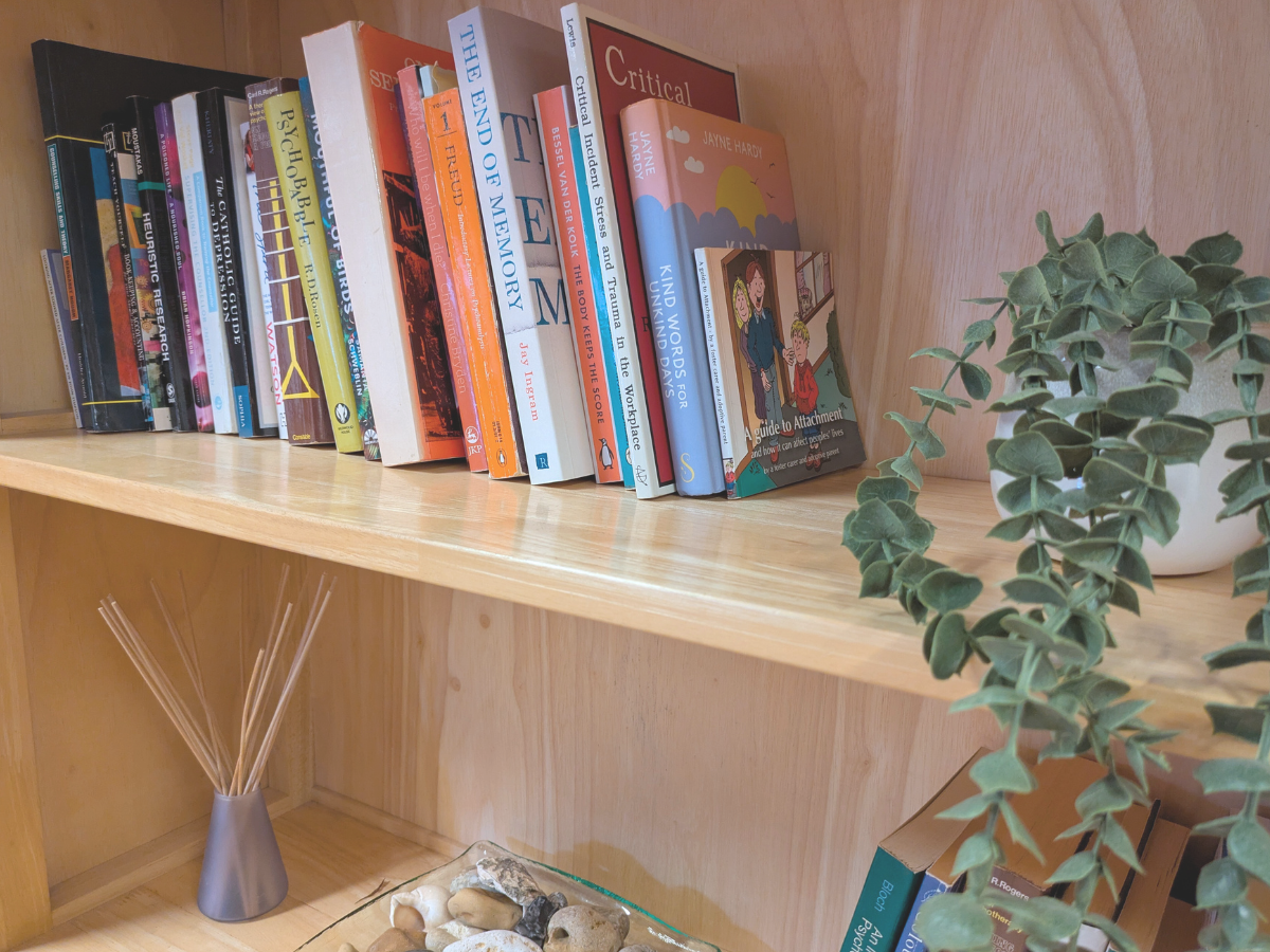 Shelf of counselling and psychology books with a green plant, representing home access to online therapy.