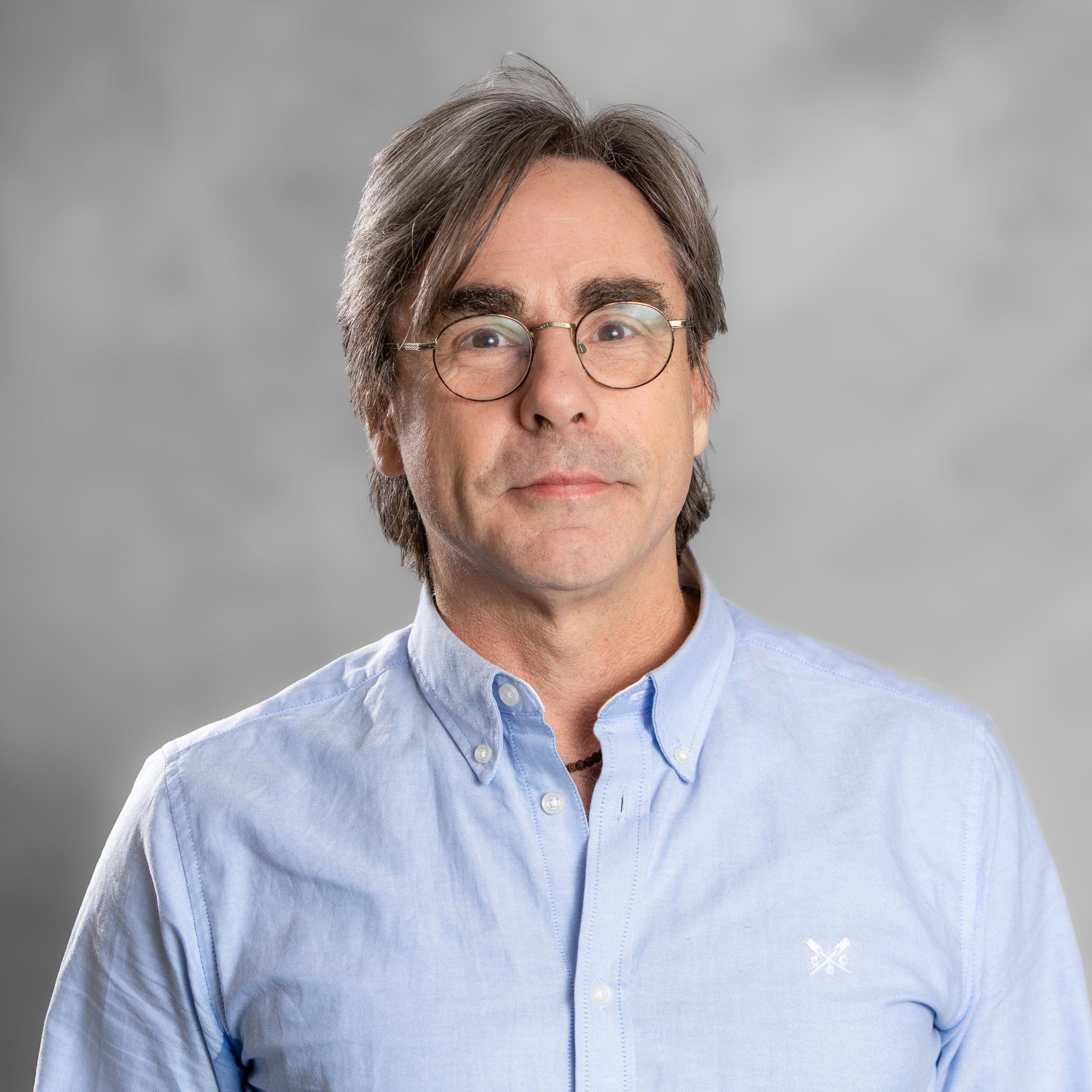 Image of Dr John O'Connor, consultant clinical psychologist for all ages specialising in trauma, depression and addiction, a man with short grey hair and glasses, he is wearing a blue shirt.