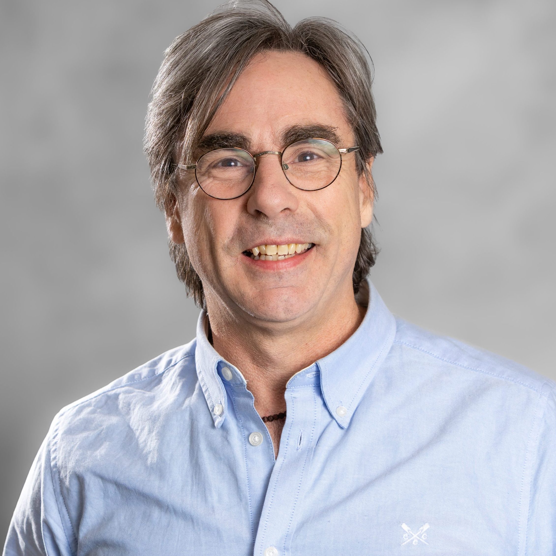 Image of Dr John O'Connor, consultant clinical psychologist for all ages specialising in trauma, depression and addiction, a man with short grey hair and glasses, he is wearing a blue shirt.