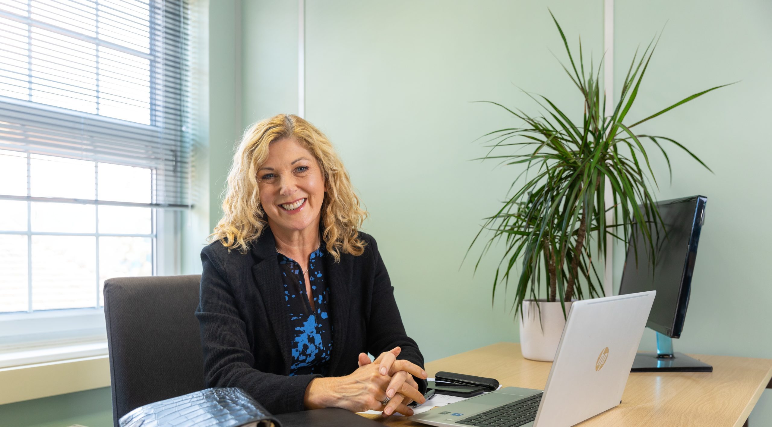 Female therapist smiling at her desk with a laptop, offering online therapy from The Eaves