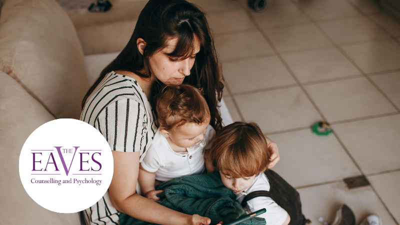 Mother and two children on a sofa watching a phone, representing maternal mental health and family wellbeing