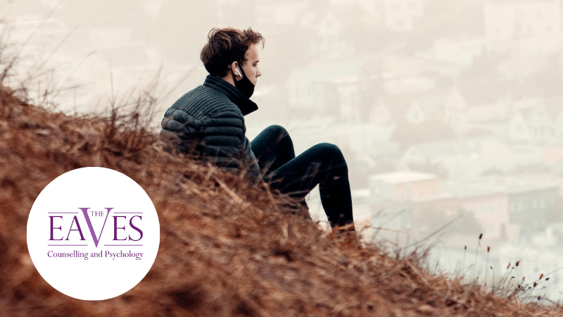 Man in running gear sitting alone on a grassy hill wearing earphones, reflecting on loneliness and mental health.