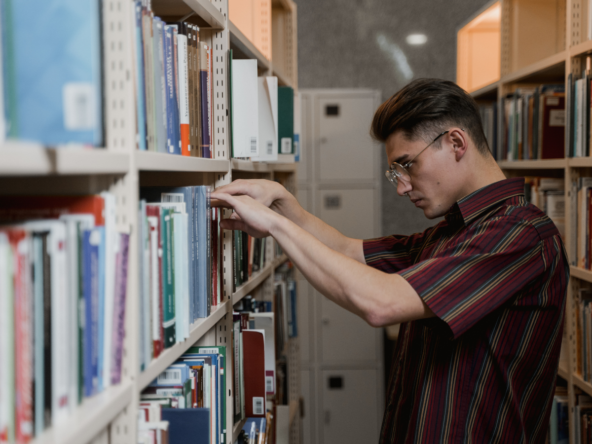 Person browsing books in a library, representing the search for meaning, purpose, and personal growth through reading.