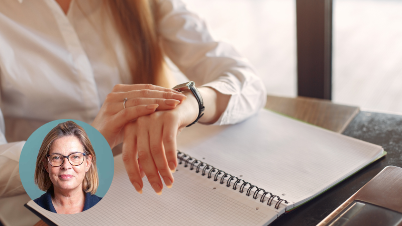 Woman at a desk looking at her watch with a notepad, reflecting time management and executive functioning challenges.