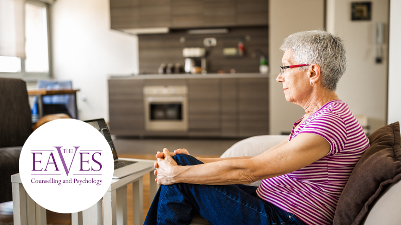 Elderly woman sitting in her living room on a video call for online therapy with The Eaves Counselling and Psychology Ltd logo in the corner.