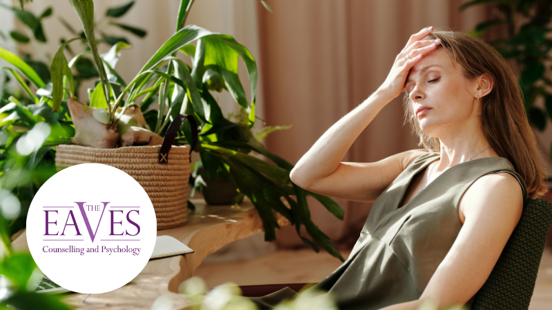 Woman sitting at a desk surrounded by greenery, resting her head on her hand and looking tired and overwhelmed.
