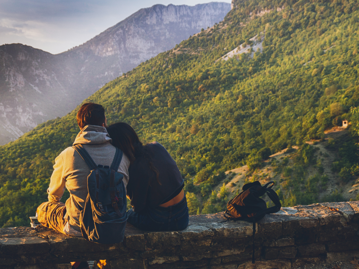 Couple standing together in the mountains, woman resting her head on her partner’s shoulder, symbolising support and connection