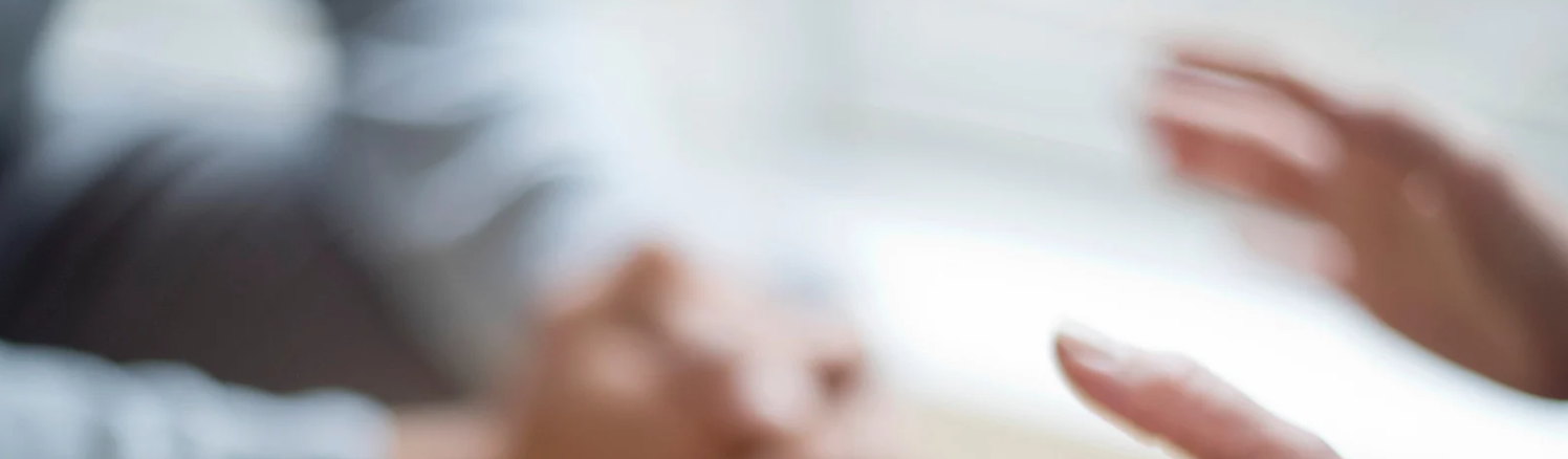 Blurry image of two people engaged in conversation. One person has their hands gesturing expressively, while the other holds their hand out. The background is out of focus, emphasising the interaction.
