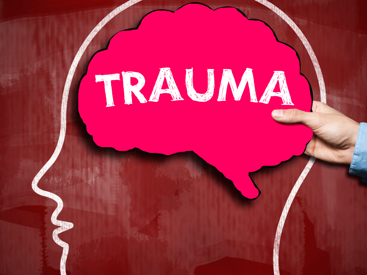 Illustration of a human head outline with a pink brain labeled TRAUMA held by a hand, set against a red background.