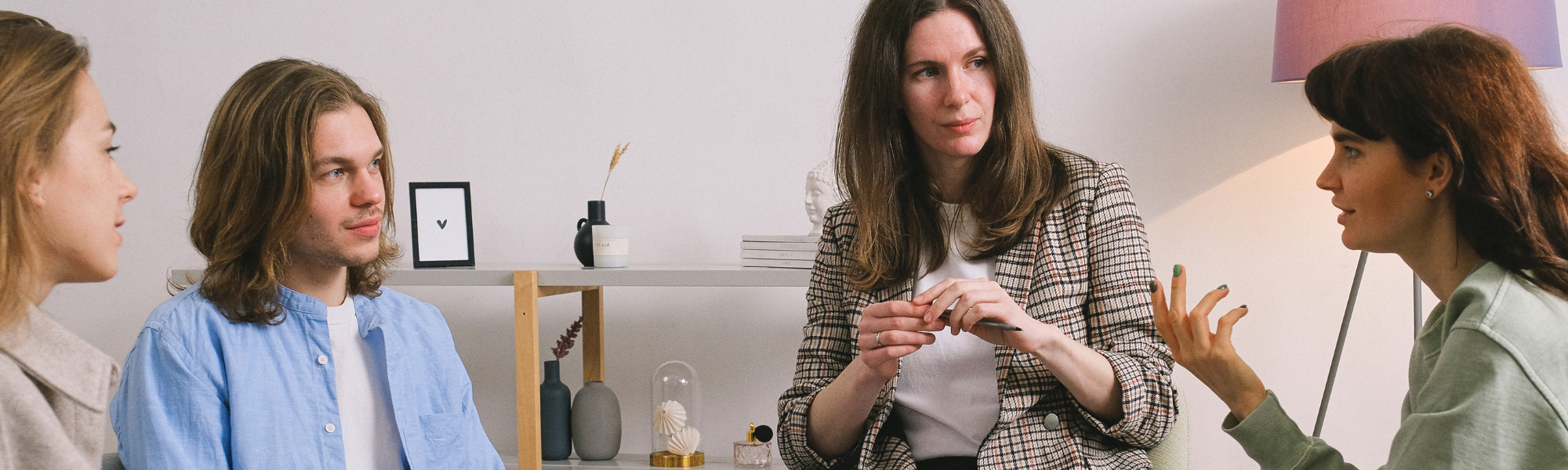 Group therapy session with three women and one man talking and listening, illustrating discussion and support in mental health treatment.