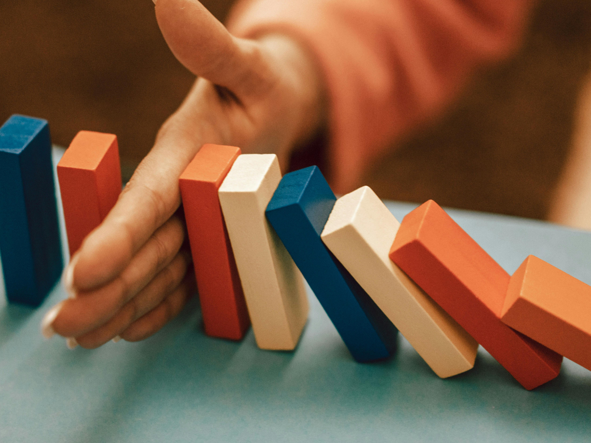 Hand stopping colorful domino blocks from falling, symbolising preventing the negative impact of mental health stigma and seeking support