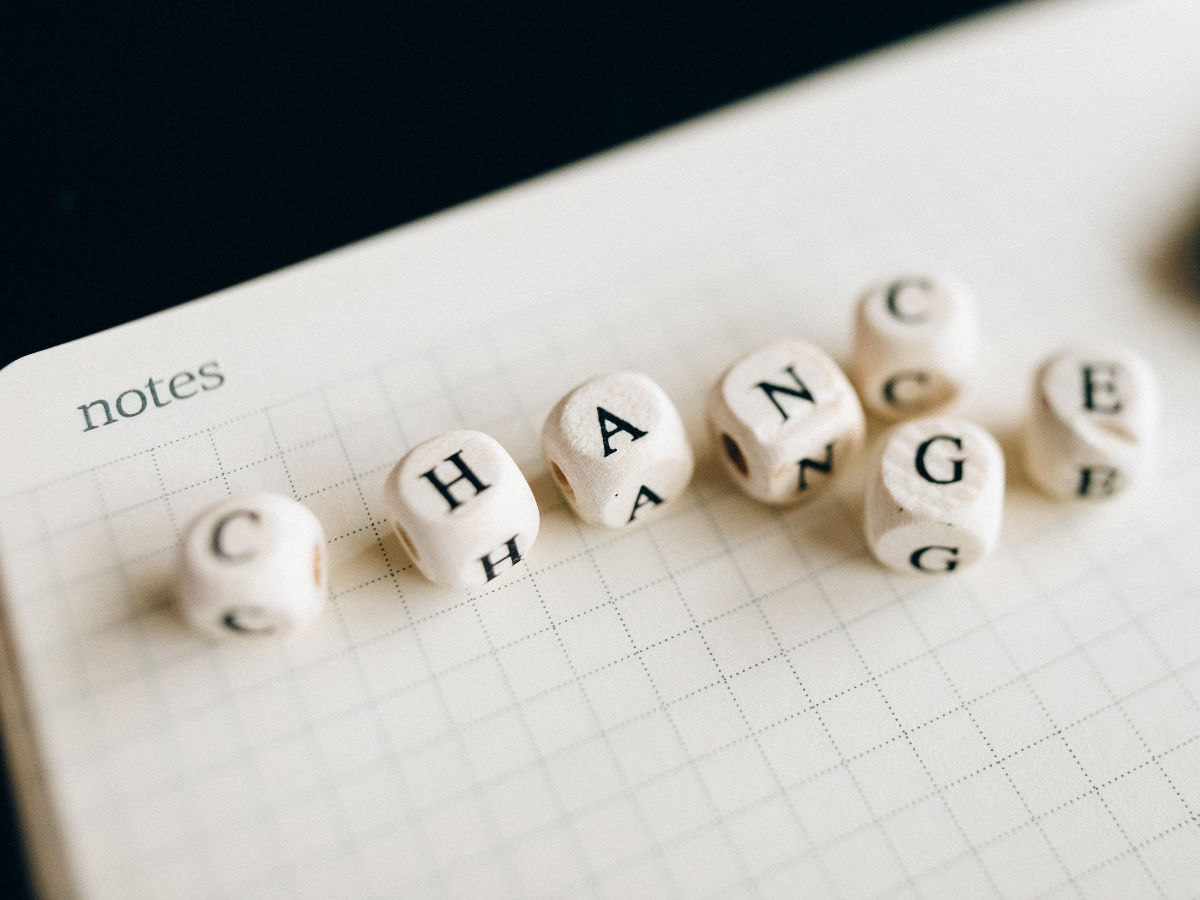 Wooden lettered cubes spell out the word CHANGE on a gridded notebook page labeled notes, with a few extra cubes scattered nearby.