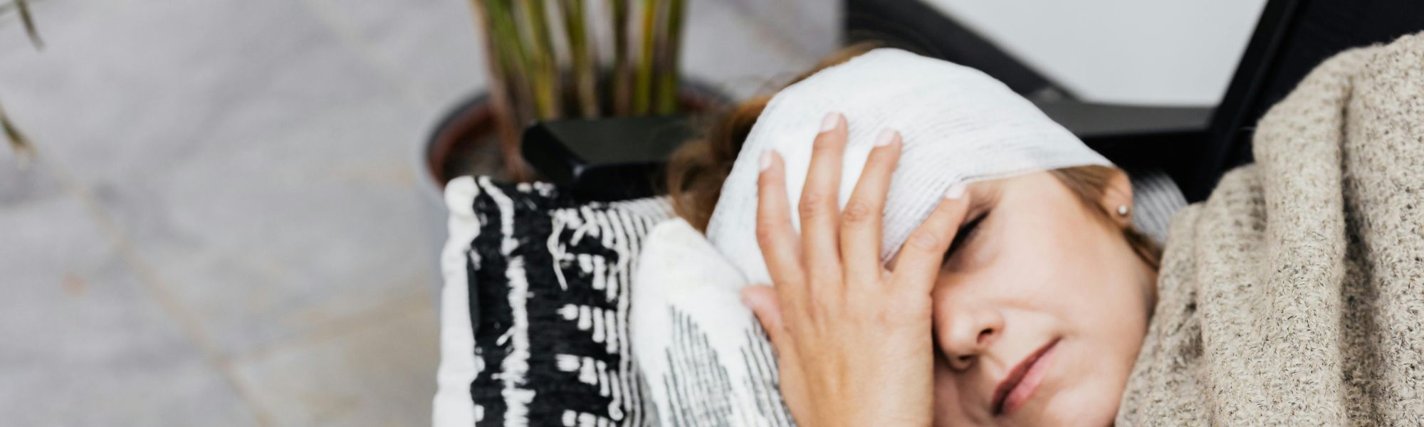 Woman resting on a sofa with a head bandage, eyes closed, with water and medication on a coffee table, representing recovery and trauma support in Surrey.