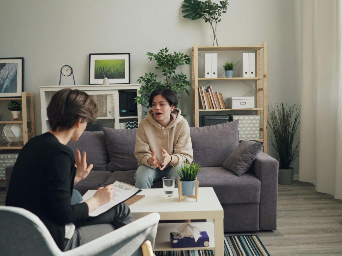 Patient and therapist sitting in a therapy room having a conversation, with grey chair, dark grey sofa, and a small coffee table, representing professional trauma support and counselling in Surrey.
