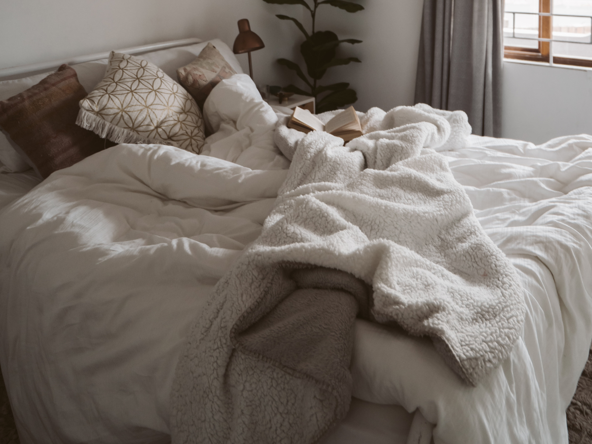 Unmade bed with a fluffy throw, side lamp, and tall house plant, symbolising rest, sleep disruption, and mental health