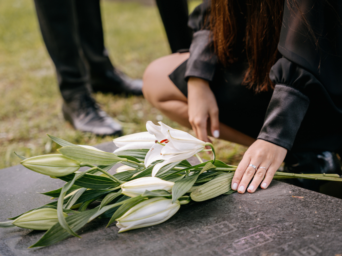 Woman placing white lilies on a grave, symbolising grief, remembrance, and bereavement support services in Surrey.