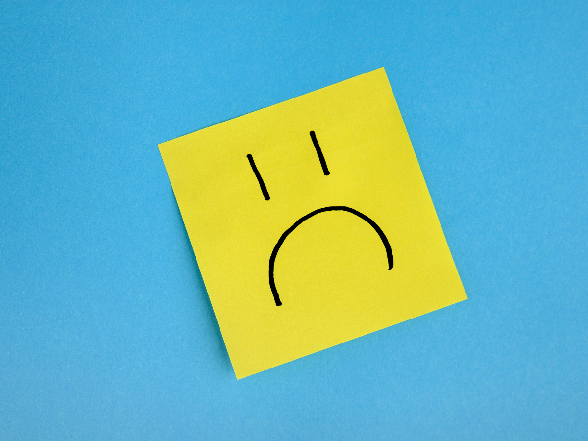 Yellow post-it note with a sad face on a blue background, representing depression and low mood in Surrey