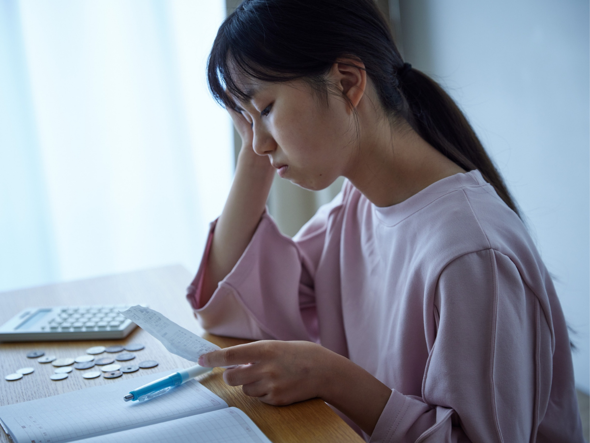 Woman sitting at a table with notebook and pen, head resting in one hand, appearing stressed or overwhelmed while trying to work