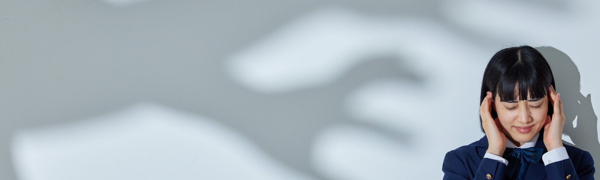 Woman holding her temples with eyes closed, shadowy hands reaching toward her, depicting anxiety and stress