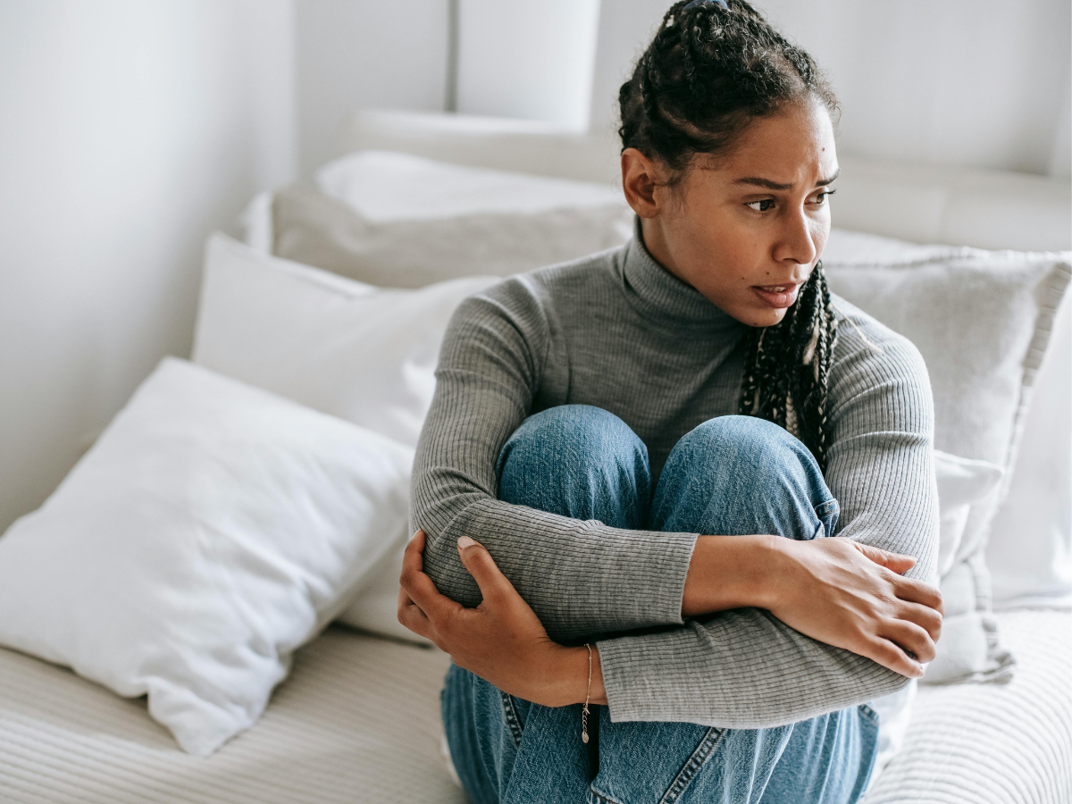 Teen sitting on a bed with knees pulled to chest, looking away, representing adolescent emotional distress