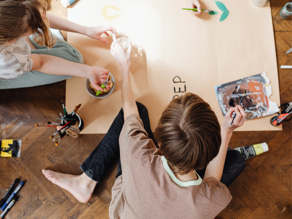 Overhead view of a child and therapist sitting on the floor at a low table, drawing and painting together during a therapy session