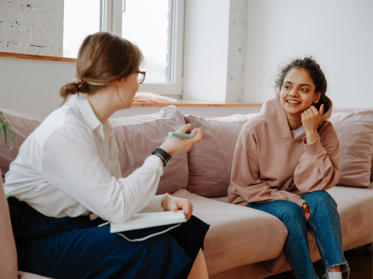 Therapist and young girl sitting on a sofa in a therapy room, having a friendly and engaging conversation