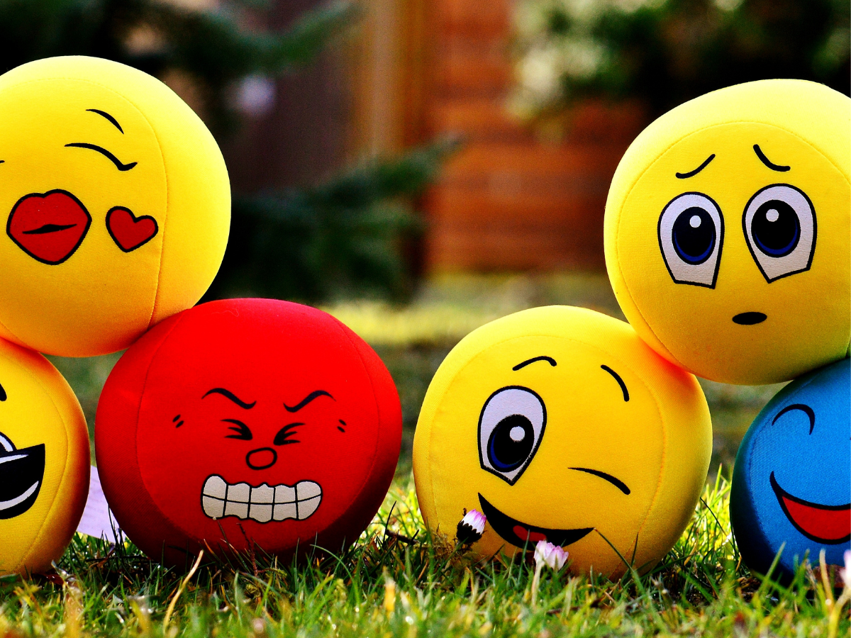 Colourful emotion balls on grass showing different facial expressions used to support emotional understanding in neurodivergent therapy.