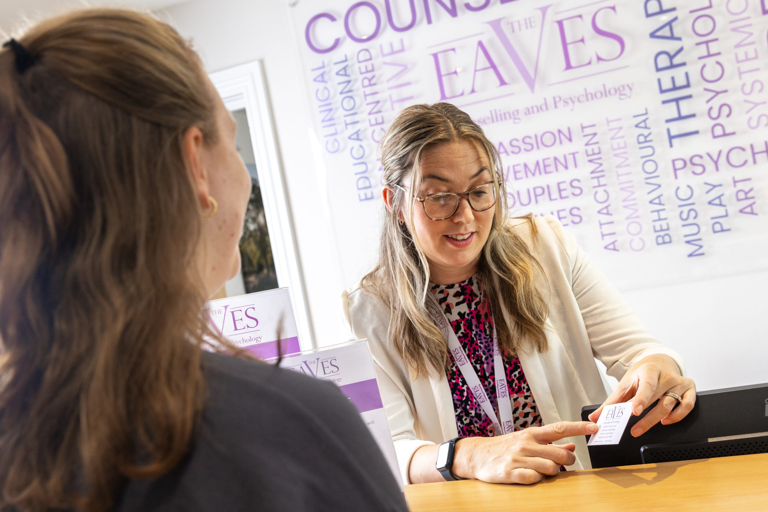 A warm and welcoming receptionist at The Eaves helping a client at the front desk.
