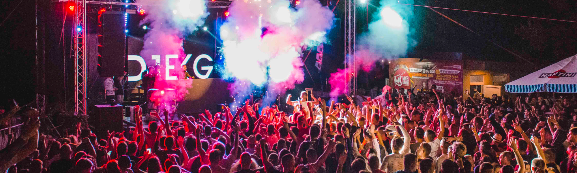 Crowd enjoying a night-time music festival with a brightly lit stage in the background, capturing the energy of a live concert.
