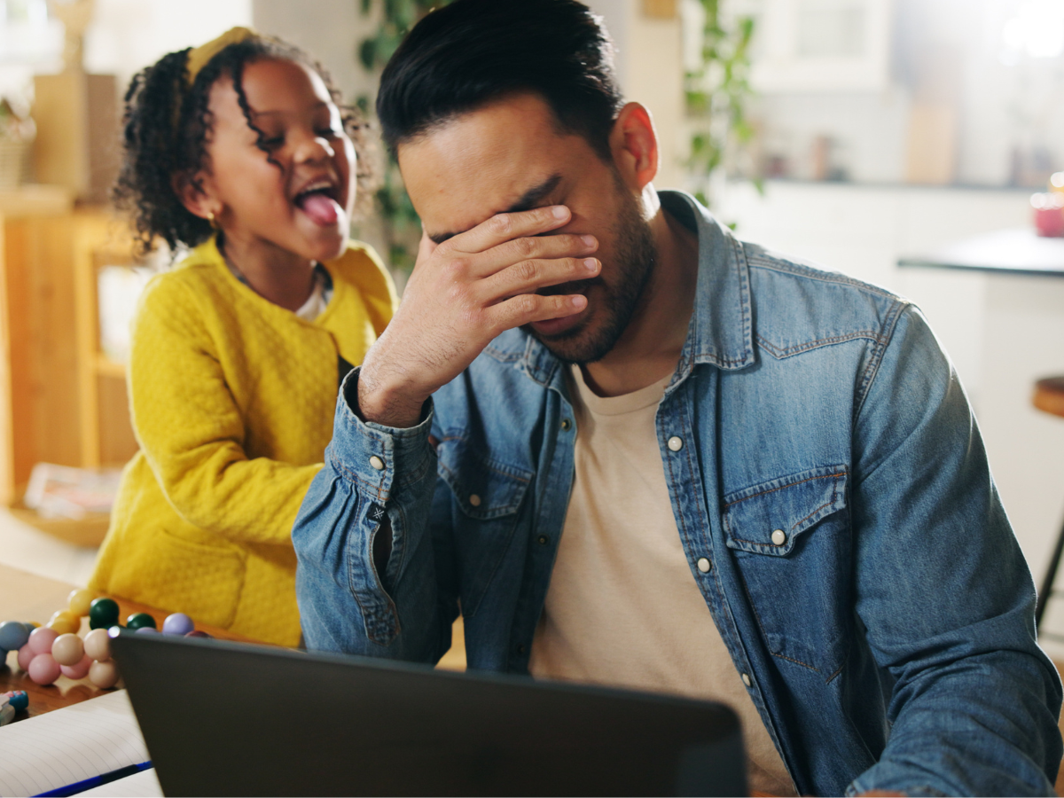 A father trying to work while his young daughter seeks his attention, illustrating parental burnout.