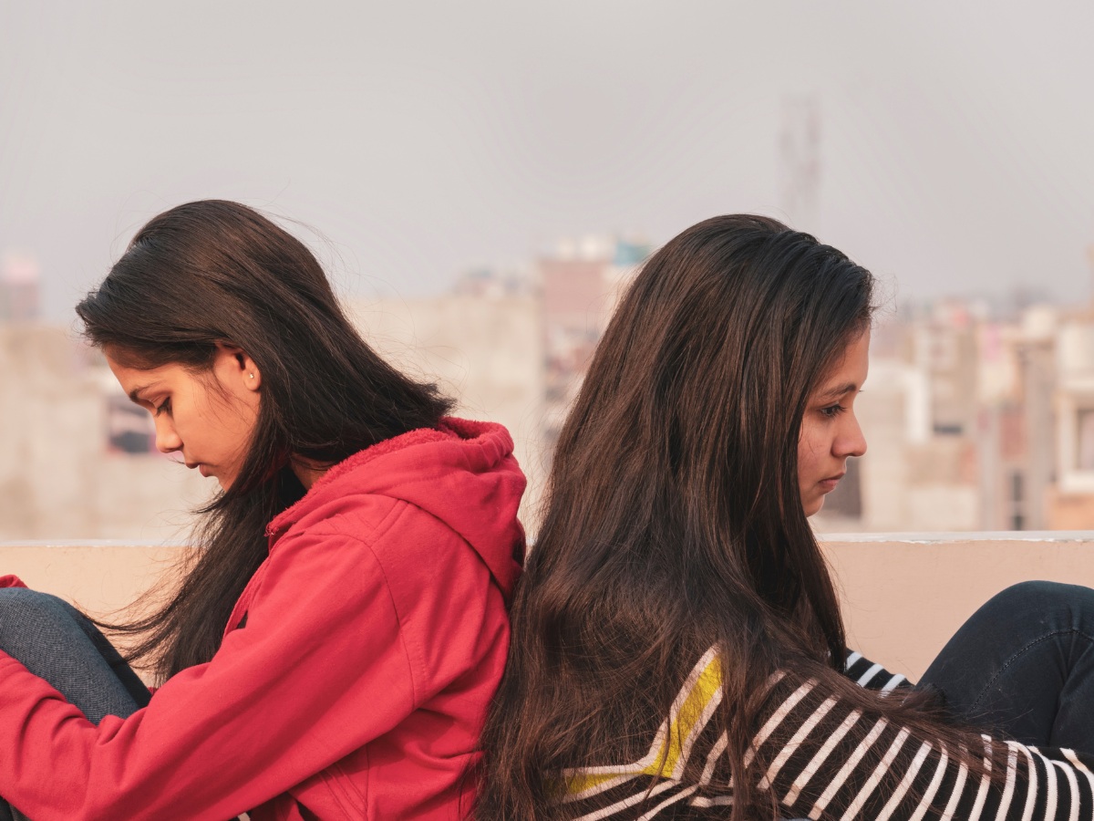 Two women sitting back to back, appearing distant and withdrawn