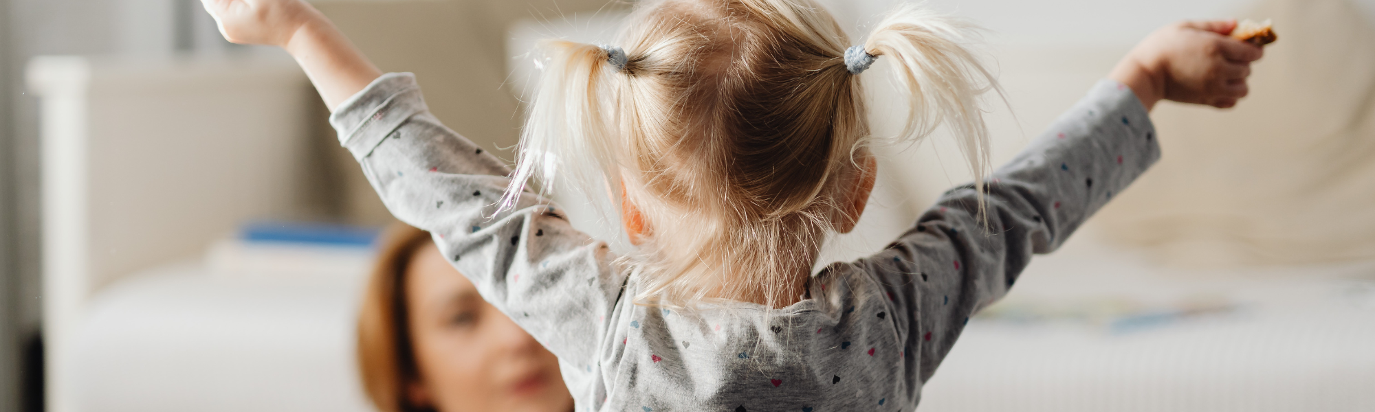 Toddler raising hands while mom sits on the floor in the background, illustrating parental burnout and parenting challenges