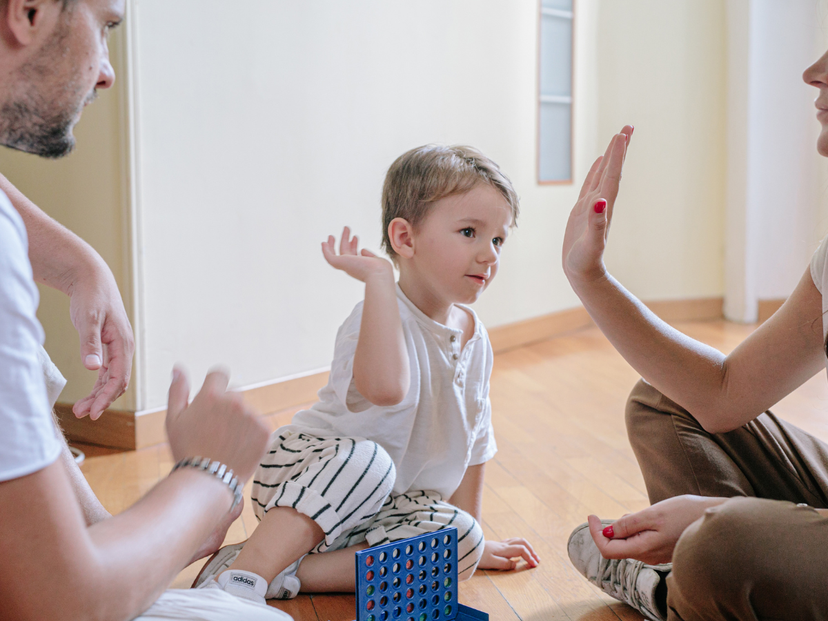 Mom, dad, and son sitting on the floor playing a board game, mom and son about to high-five, showing family bonding and joyful parenting
